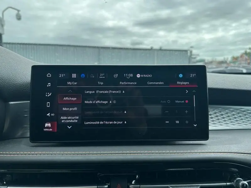 Écran tactile central de l'Alfa Romeo Tonale 2025 affichant les réglages de luminosité dans un intérieur noir avec surpiqûres beige.