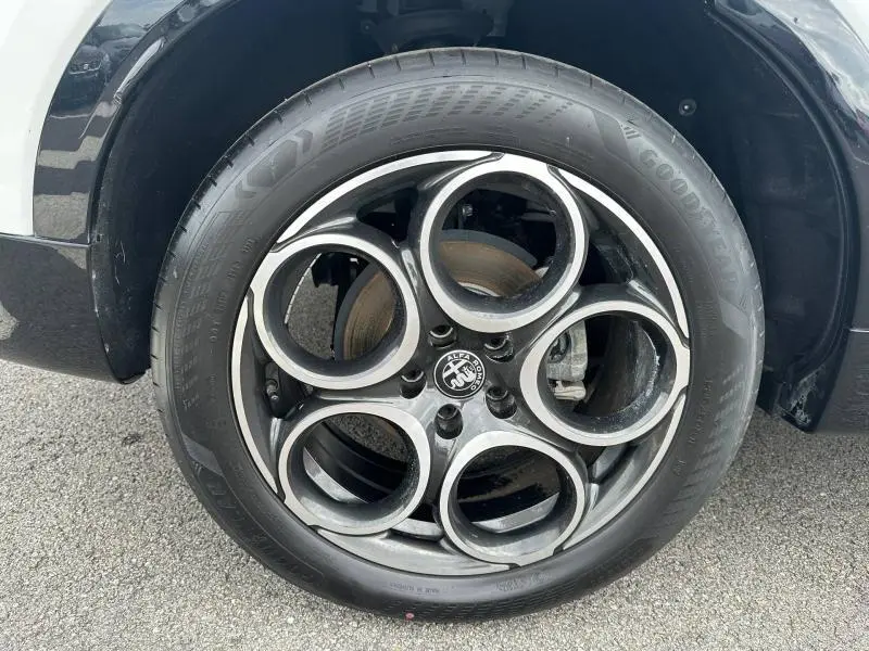 Gros plan sur la jante alu noire et argentée à cinq cercles de l'Alfa Romeo Tonale blanc Monterosa pastel, côté avant droit.