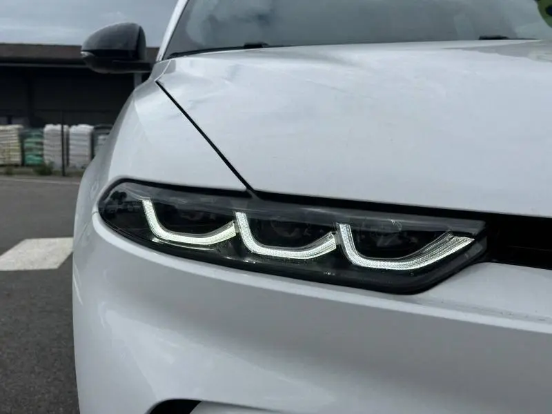 Gros plan sur le phare avant gauche allumé de l'Alfa Romeo Tonale blanc Monterosa Pastel, soulignant son design LED distinctif.