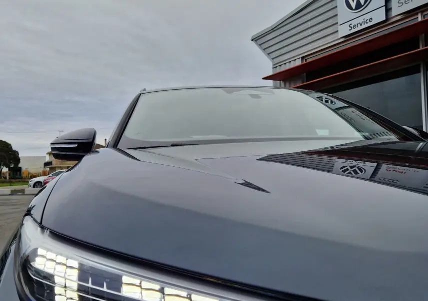 Gros plan sur le phare avant gauche allumé d'un Audi Q6 e-tron Performance S-Line gris Manhattan, vue en légère contre-plongée.