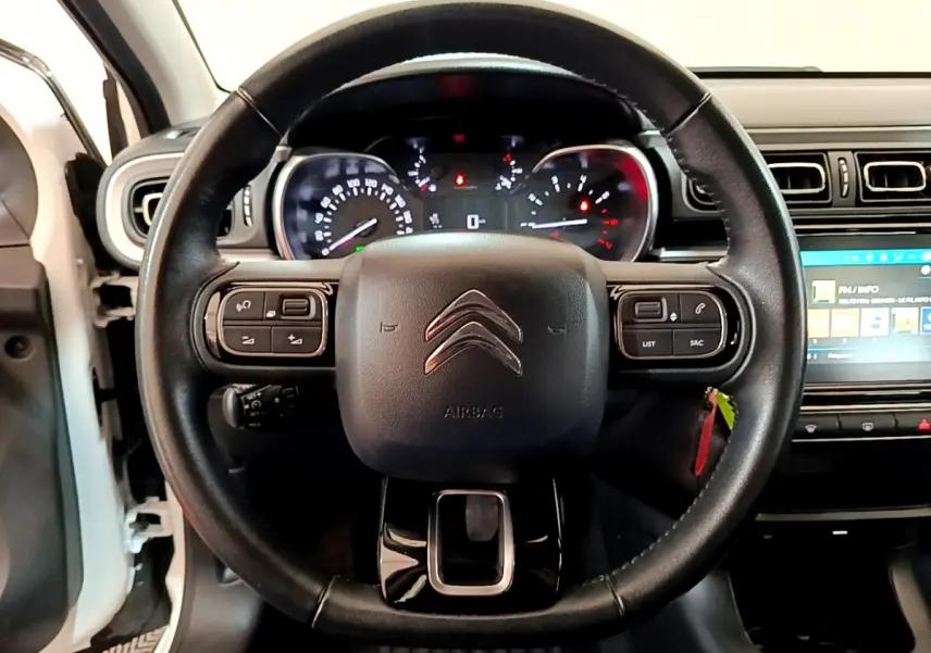 Vue rapprochée du volant cuir noir de la Citroën C3 blanche 2019 avec commandes intégrées et tableau de bord éclairé.