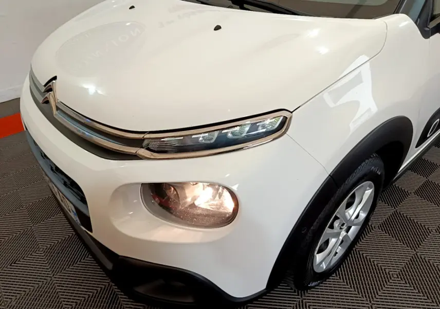 Vue 3/4 avant droit d'une Citroën C3 blanche avec phares allumés et jantes alliage visibles