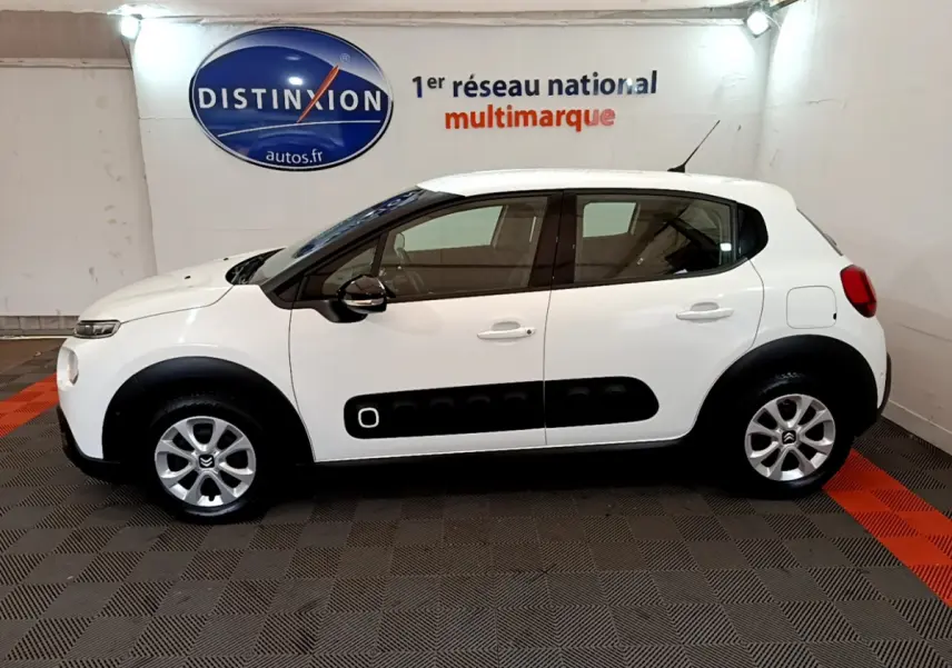 Profil droit d'une Citroën C3 blanche de 2019 avec protections noires sur les portières, en intérieur showroom.