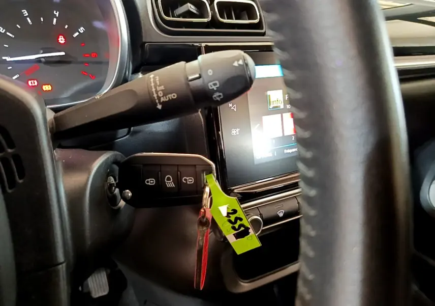 Vue rapprochée du tableau de bord et volant cuir noir d'une Citroën C3 blanche, avec clé insérée et écran tactile allumé.