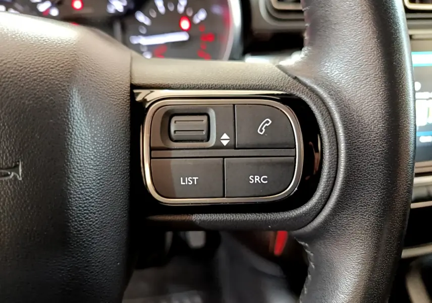 Gros plan sur les commandes gauche du volant cuir de la Citroën C3 blanche, avec boutons de gestion audio et appels.