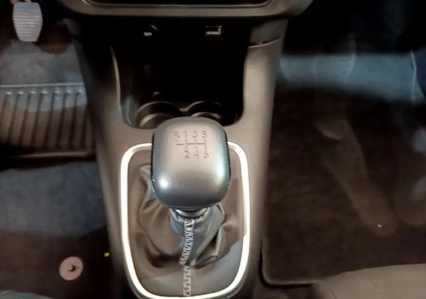 Le levier de vitesses manuel noir de la Citroën C3 blanche vu de dessus, entouré d'une garniture argentée.