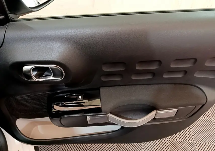 Vue rapprochée de la porte intérieure côté conducteur d'une Citroën C3 blanche, avec poignée et commandes noires.