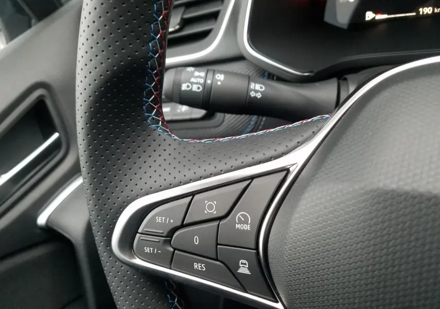 Gros plan sur le volant perforé du Renault Captur gris Rafale, mettant en valeur les commandes de régulateur adaptatif.