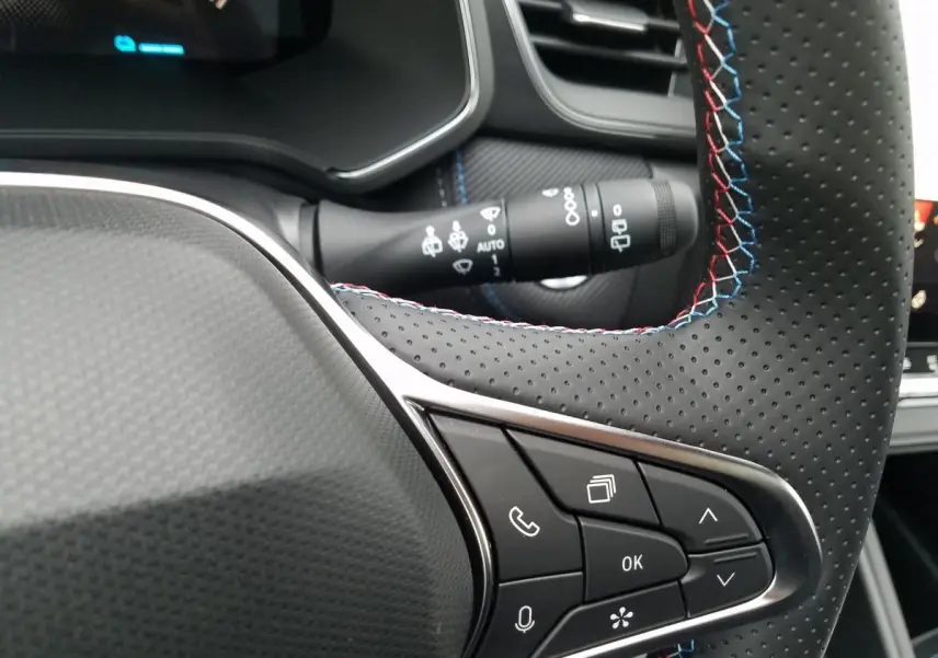 Détail du volant perforé avec surpiqûres tricolores et commandes intégrées dans un Renault Captur gris Rafale 2025.