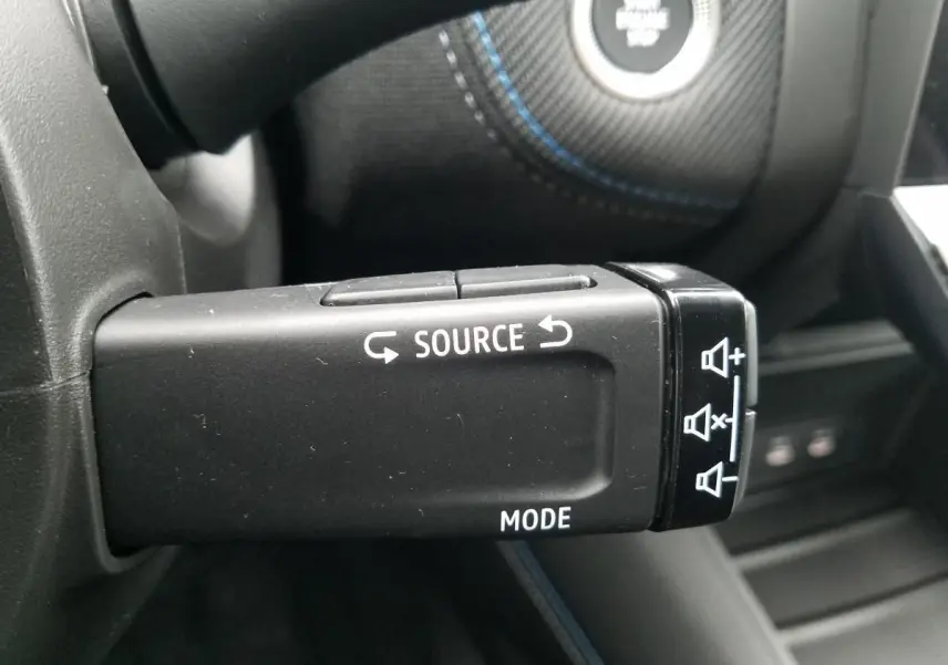 Gros plan sur la commande au volant du Renault Captur 2025, avec boutons source et mode visibles sur fond noir.