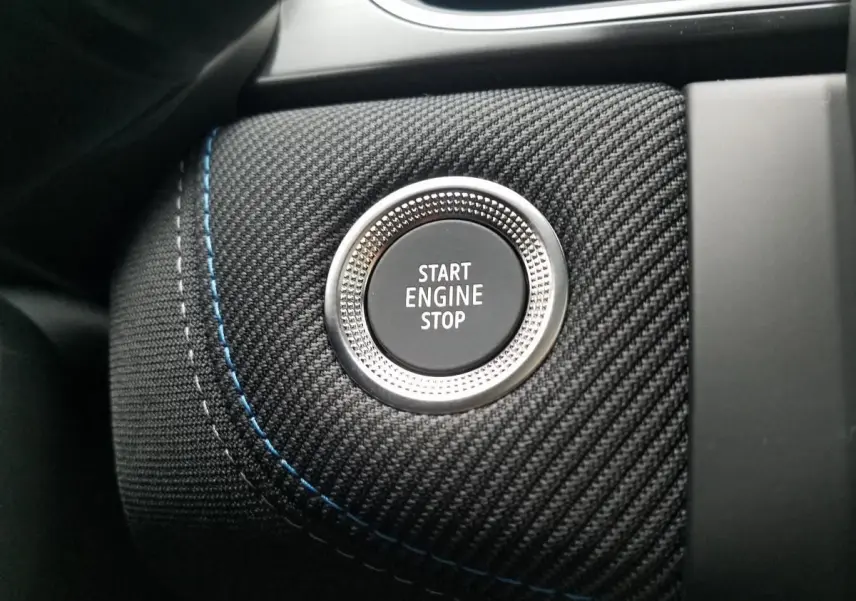 Gros plan sur le bouton Start Engine Stop entouré de tissu noir texturé avec surpiqûres bleues dans un Renault Captur 2025.