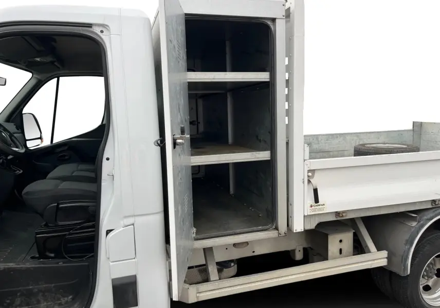 Vue latérale gauche d'un Renault Master blanc 2023 avec cabine ouverte et coffre métallique de rangement visible sur la benne.