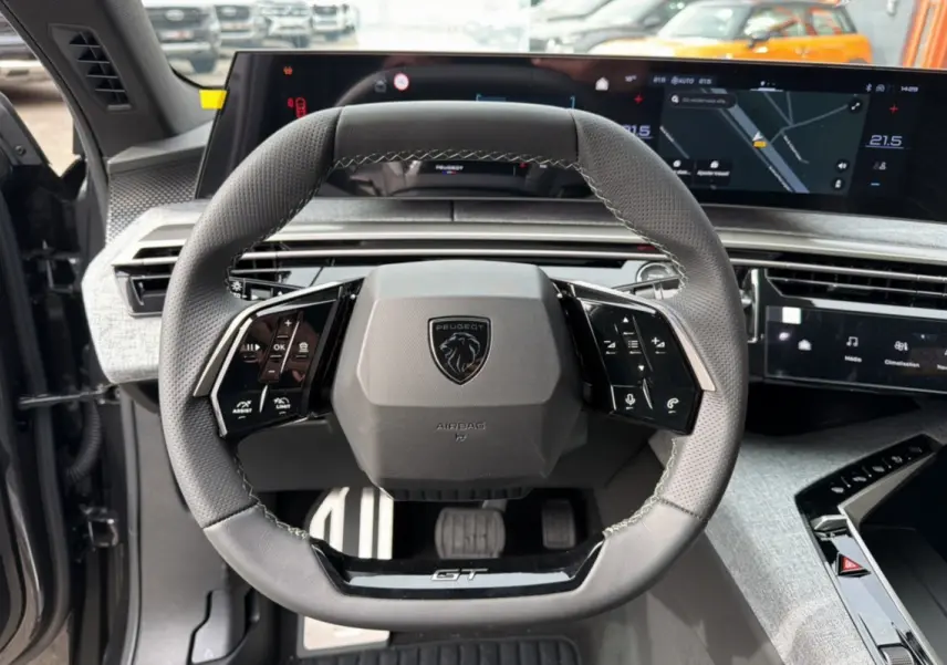Vue rapprochée du volant cuir multifonctions Peugeot 3008 Hybrid GT 2025 avec tableau de bord numérique et pédalier aluminium.
