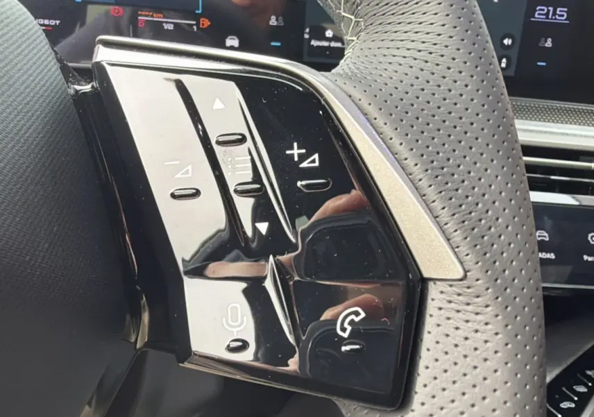 Gros plan sur les commandes noires brillantes du volant cuir perforé du Peugeot 3008 Hybrid gris titane.
