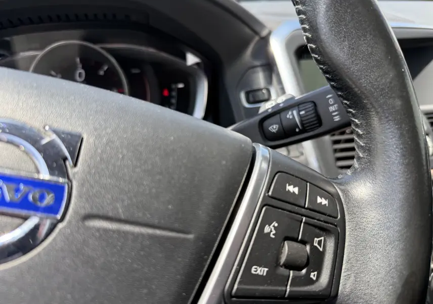 Gros plan sur le volant en cuir noir du Volvo XC60 2016, avec commandes audio et logo Volvo visible au centre.