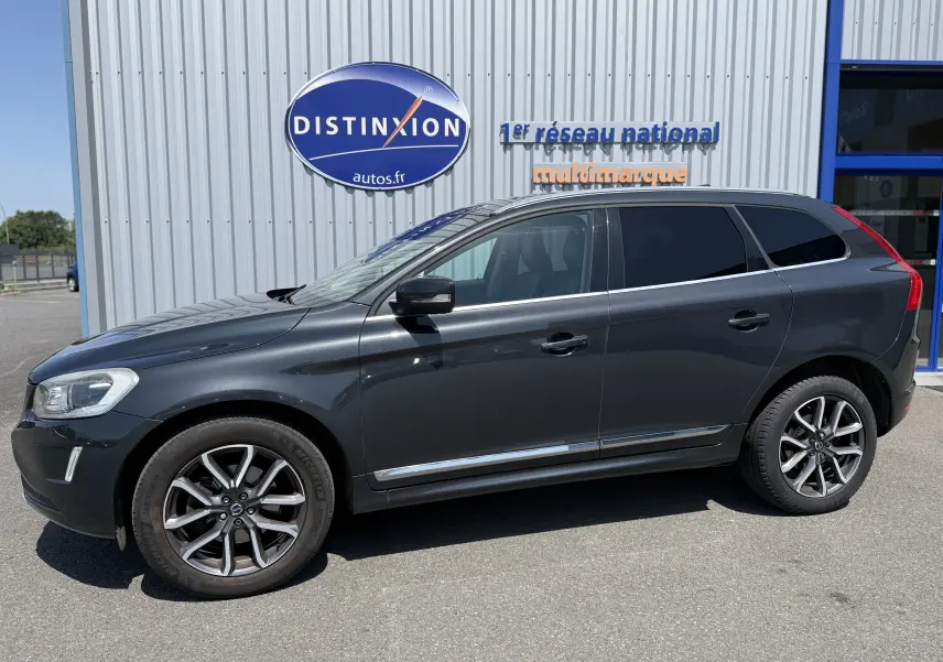 Vue de profil côté gauche d’un Volvo XC60 gris foncé garé devant un bâtiment avec logo Distinxion.