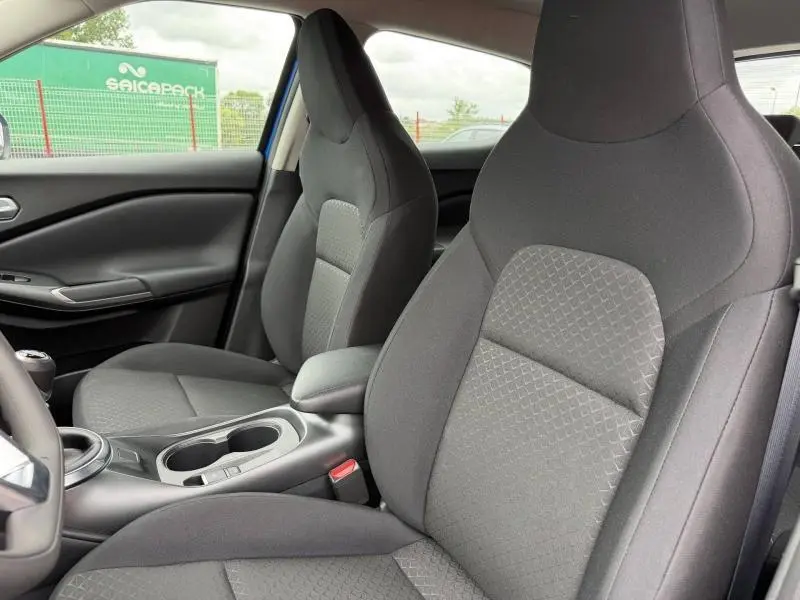 Intérieur de Nissan Juke 2025 vu côté droit, sièges tissu noir avec console centrale et porte-gobelets.