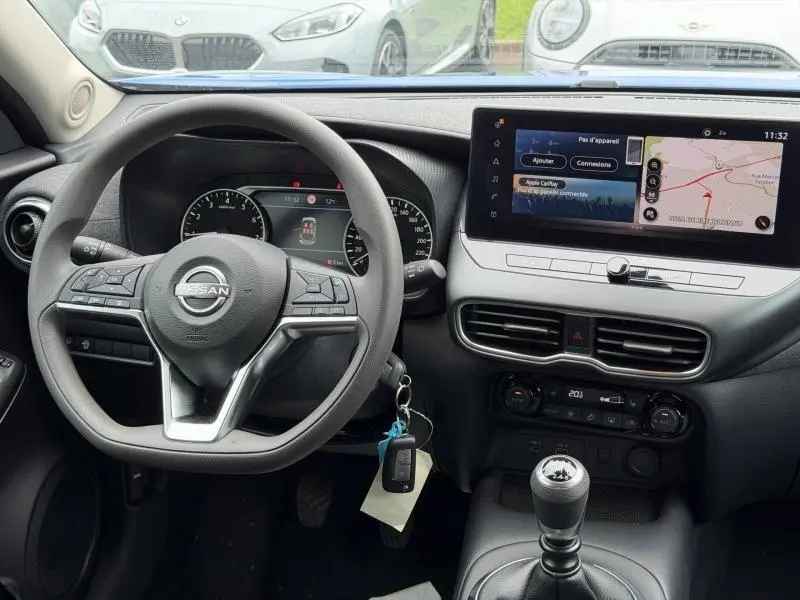 Vue intérieure du tableau de bord du Nissan Juke 2025 avec volant multifonction, écran tactile et levier de vitesse manuel.