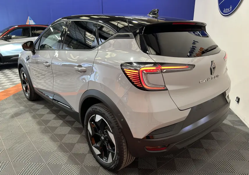 Vue 3/4 arrière droite du Renault Captur gris Rafale avec toit noir et feux arrière LED allumés en intérieur showroom.