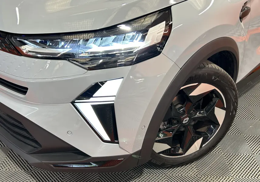 Gros plan sur l’avant droit du Renault Captur gris Rafale, mettant en valeur le phare LED et la jante noire à design étoilé.