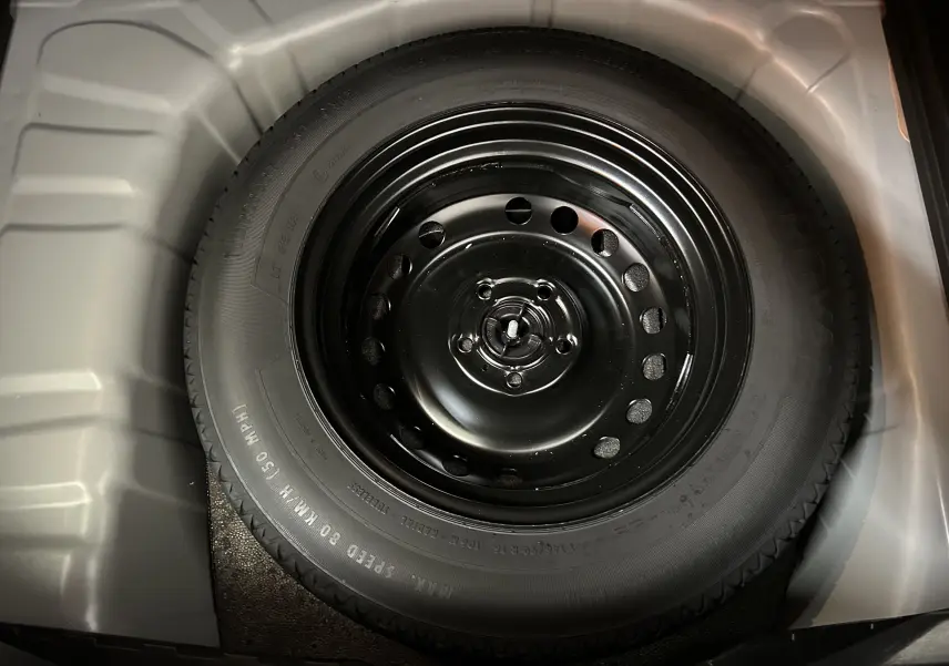 Gros plan sur la roue de secours noire dans le coffre du Renault Captur gris Rafale, vue de dessus.