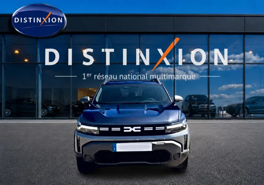 Vue avant d'un Dacia Duster gris schiste avec calandre lumineuse et logo distinctif, devant une vitrine Distinxion.