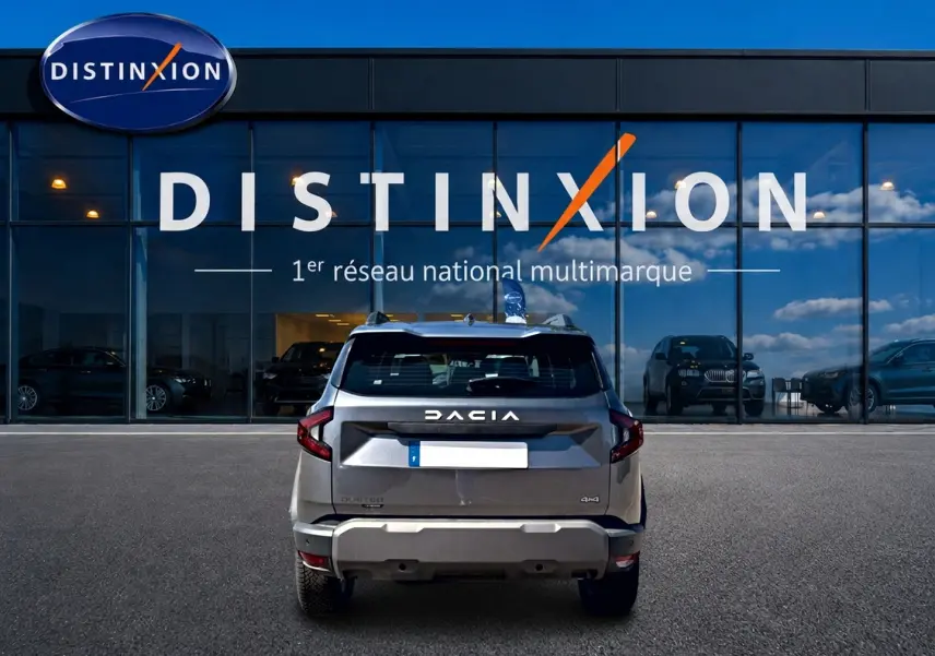Vue arrière d'un Dacia Duster gris schiste 2026 garé devant une vitrine avec logo Distinxion.