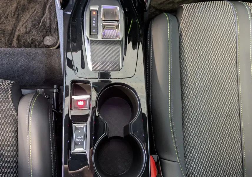 Vue plongeante sur la console centrale noire brillante de la Peugeot 208 Hybrid 145ch GT avec sièges gris à surpiqûres vertes.