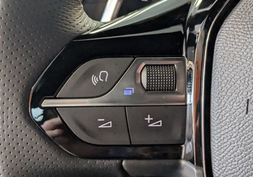 Gros plan sur les commandes gauche du volant de la Peugeot 208 Hybrid 145ch GT gris Artens, avec molette et boutons de volume.