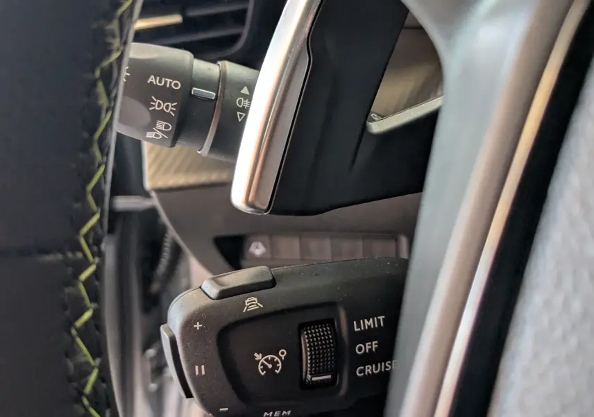 Gros plan sur la commande de régulateur de vitesse et feux, volant avec surpiqûres vertes, intérieur Peugeot 208 gris Artens.
