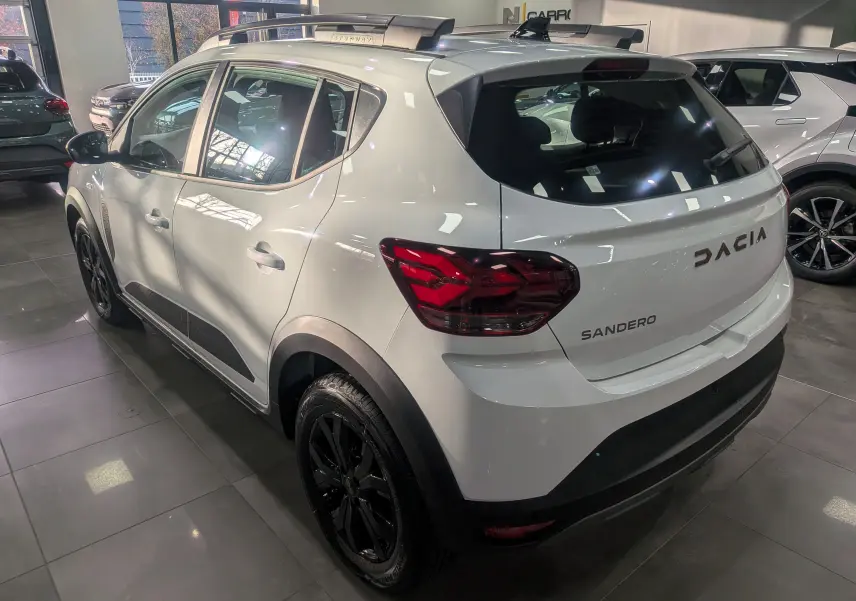 Vue 3/4 avant gauche d'une Dacia Sandero Stepway TCe 110 blanc glacier avec jantes noires en showroom.