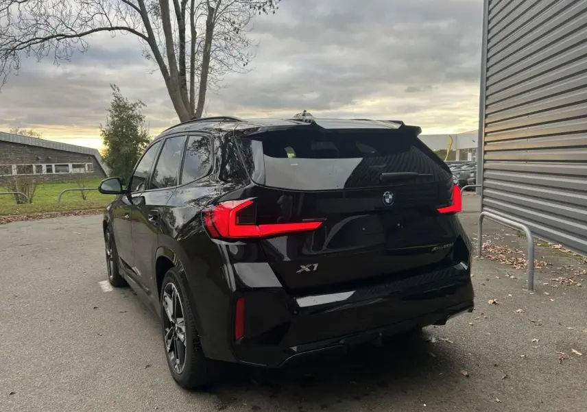 Vue 3/4 arrière gauche d'un BMW X1 2025 noir Saphir avec feux arrière LED et jantes M Sport.
