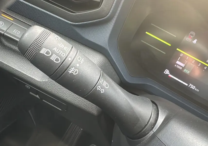 Gros plan sur la commande des feux et clignotants du tableau de bord du Dacia Duster 2025, intérieur noir.
