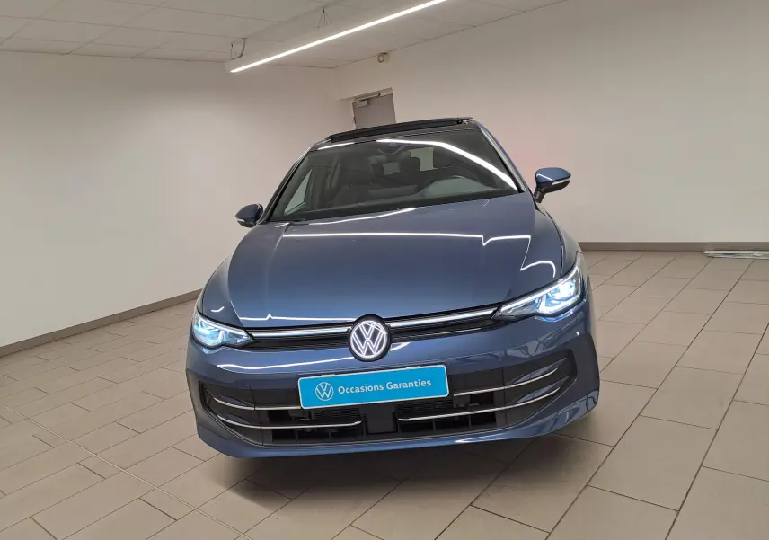 Volkswagen Golf 2024 bleu Anémone vue de face en intérieur avec projecteurs Matrix LED allumés et toit ouvrant.