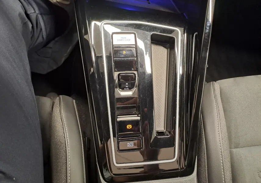 Vue rapprochée de la console centrale noire brillante de la Volkswagen Golf 1.5 eTSI 2024 avec commandes de boîte auto.