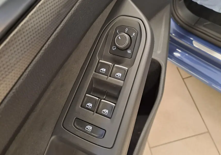 Vue rapprochée des commandes de lève-vitres et rétroviseurs sur la porte côté conducteur d'une Volkswagen Golf Bleu Anémone.