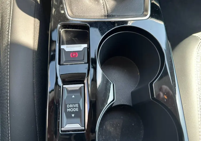 Gros plan sur la console centrale noire brillante de la Peugeot 208 2025, avec boutons frein électrique et mode de conduite.