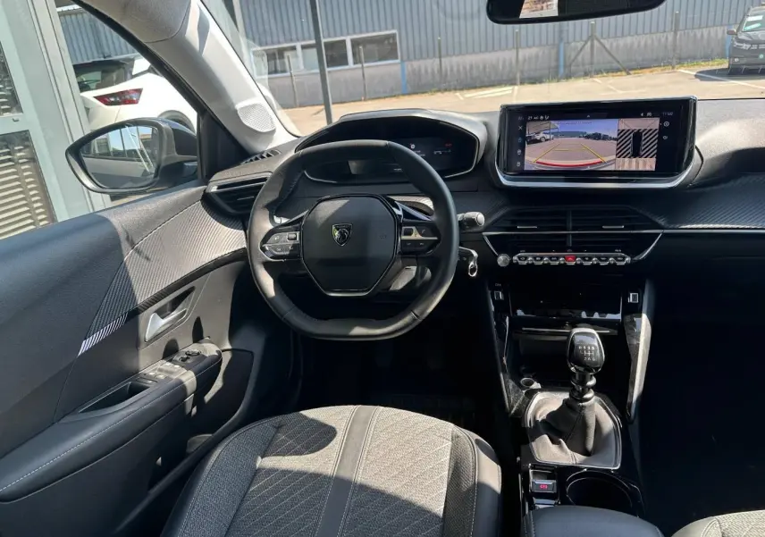 Vue intérieure avant de la Peugeot 208 1.2 100ch gris Selenium, volant compact et écran tactile avec caméra de recul.