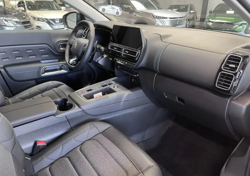 Intérieur avant du Citroën C5 Aircross 2025, vue côté conducteur, tableau de bord noir avec surpiqûres bleues et écran tactile central.