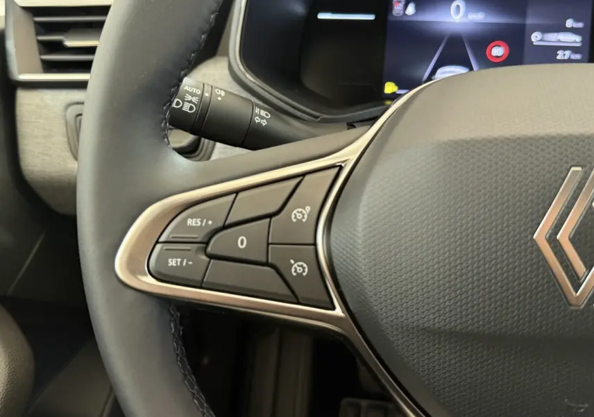 Gros plan sur le volant multifonctions noir de la Renault Clio 2025 avec commandes de régulateur de vitesse et tableau de bord numérique.