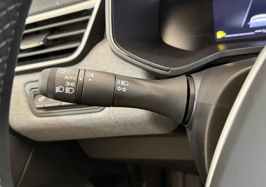 Gros plan sur la commande des phares et clignotants dans l'habitacle gris clair de la Renault Clio noire 2025.