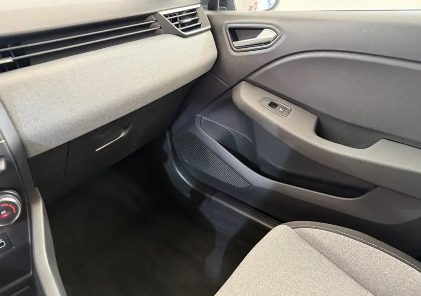 Intérieur de la Renault Clio 2025, vue côté passager avant, tableau de bord gris clair et porte noire.