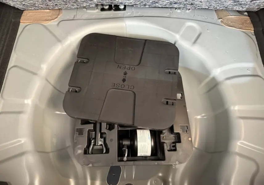 Vue plongeante sur le compartiment de rangement sous le plancher du coffre de la Renault Clio noire 2025.