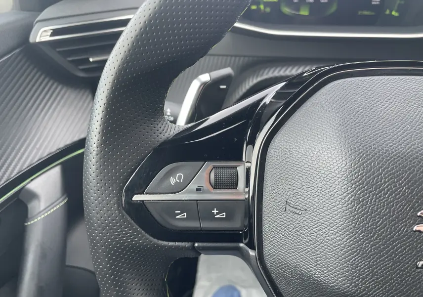 Gros plan sur le volant cuir perforé noir du Peugeot 2008 2022, avec commandes intégrées et tableau de bord numérique en arrière-plan.