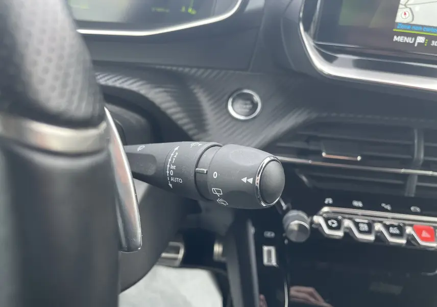 Gros plan sur la commande d’essuie-glace à gauche du volant dans l’habitacle noir du Peugeot 2008 gris Artense 2022.