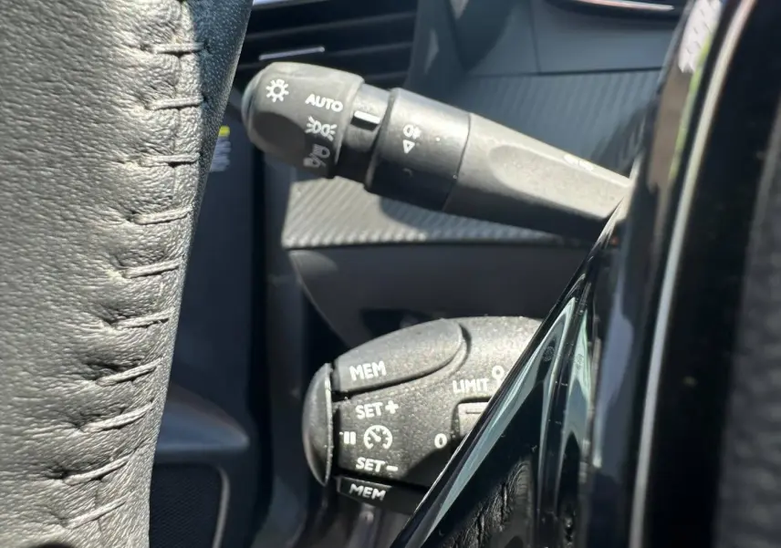 Détail des commandes au volant côté gauche sur Peugeot 208 1.2 100ch gris Selenium avec volant cuir noir.