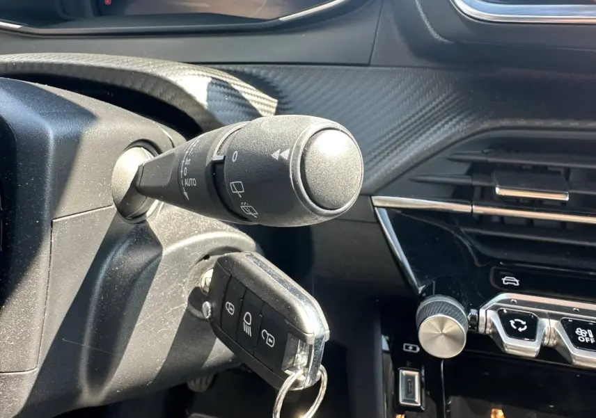 Gros plan sur le contacteur avec clé insérée et partie gauche du tableau de bord noir brillant de la Peugeot 208 gris Selenium.