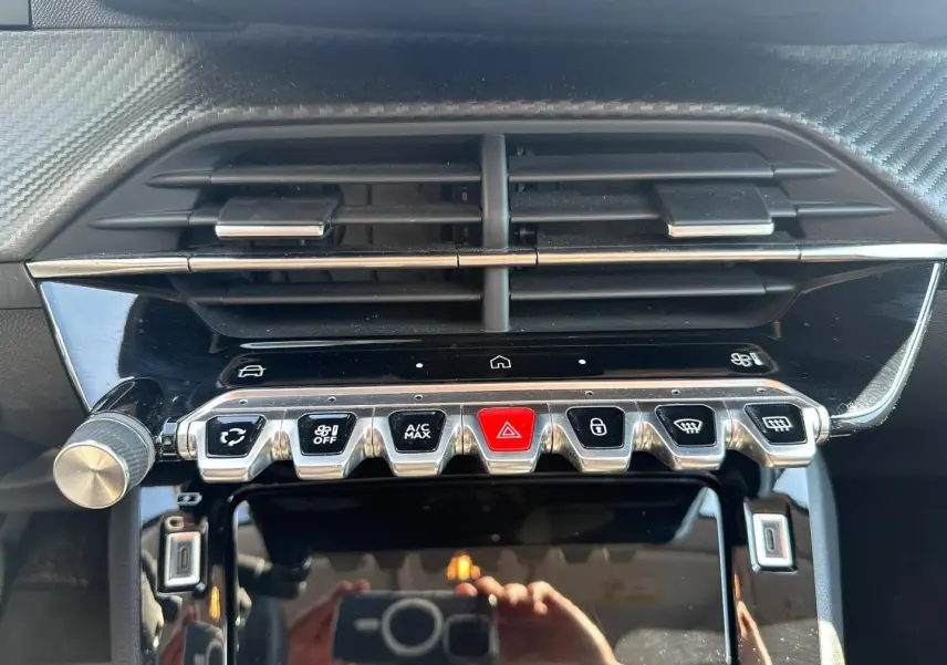 Vue rapprochée de la console centrale noire brillante de la Peugeot 208 2025 avec boutons argentés et rouge d'alerte.