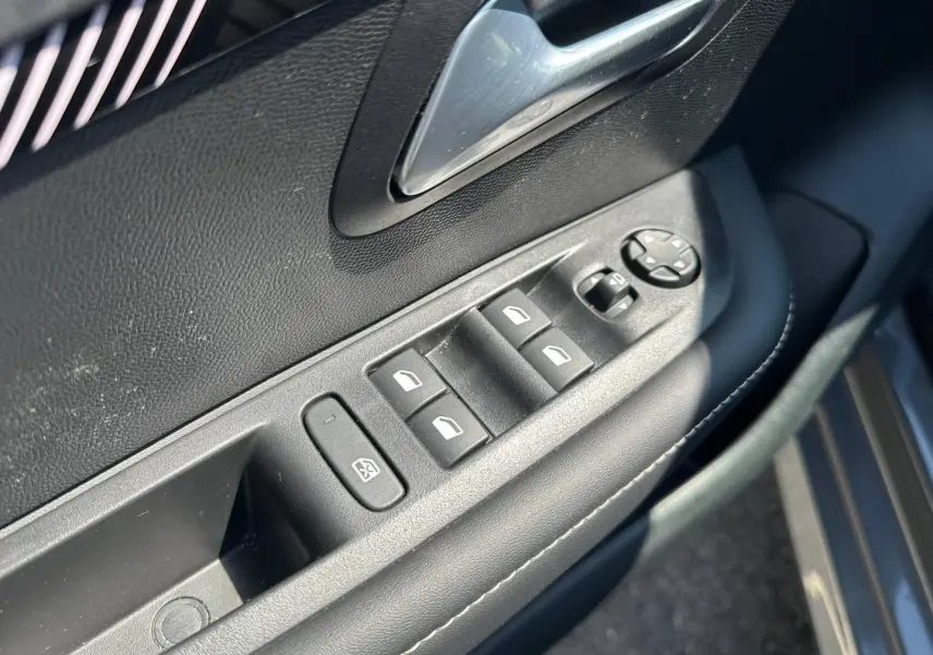 Gros plan sur la commande des vitres électriques côté gauche d’une Peugeot 208 gris Selenium avec poignée argentée.