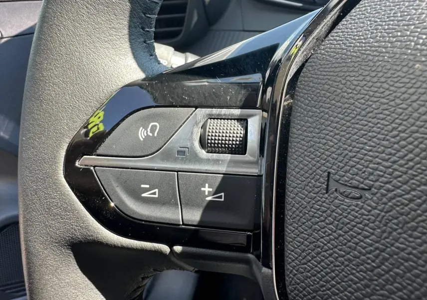 Gros plan sur les commandes du volant à gauche en plastique noir brillant de la Peugeot 208 2025, finition Gris Selenium.